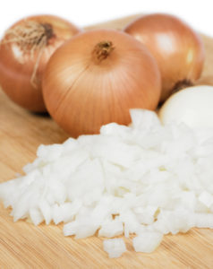 Whole onions and chopped onions on wooden chopping board